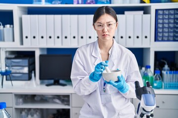 Chinese young woman working at scientist laboratory mixing skeptic and nervous, frowning upset because of problem. negative person.
