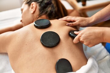 Two women therapist and patient having back massage session using black stones at beauty center