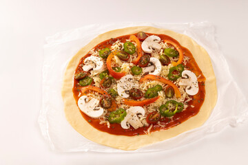 Pizza dough with tomato, mushrooms sauce, and grated cheese on baking paper
