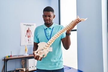 African american man holding anatomical model of spinal column skeptic and nervous, frowning upset because of problem. negative person.