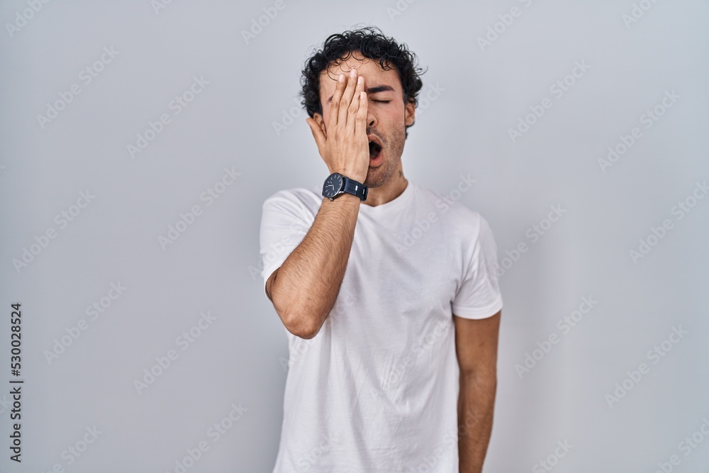 Sticker hispanic man standing over isolated background yawning tired covering half face, eye and mouth with 