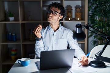 Hispanic man working at the office at night doing money gesture with hands, asking for salary payment, millionaire business