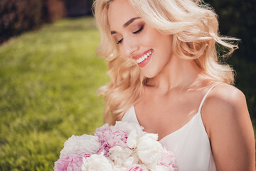 Obraz na płótnie Canvas Photo of shiny pretty young wavy woman wear white top admiring flowers enjoying sunshine outside city park