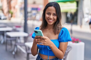 Young hispanic woman smiling confident using smartphone at street