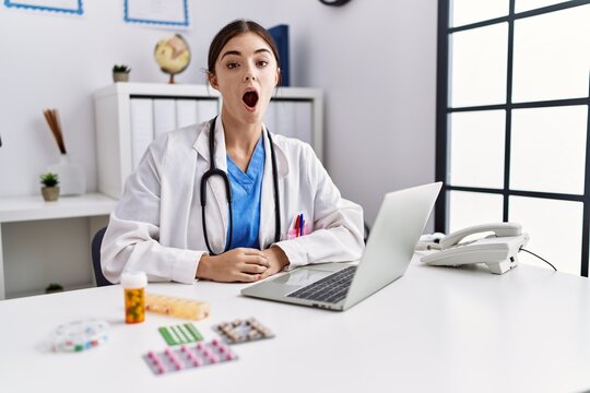 Young hispanic doctor woman wearing doctor uniform working at the clinic scared and amazed with open mouth for surprise, disbelief face