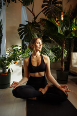 The girl does yoga against the background of green plants in his studio