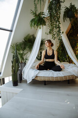 A girl on a double bed in black clothes among pillows