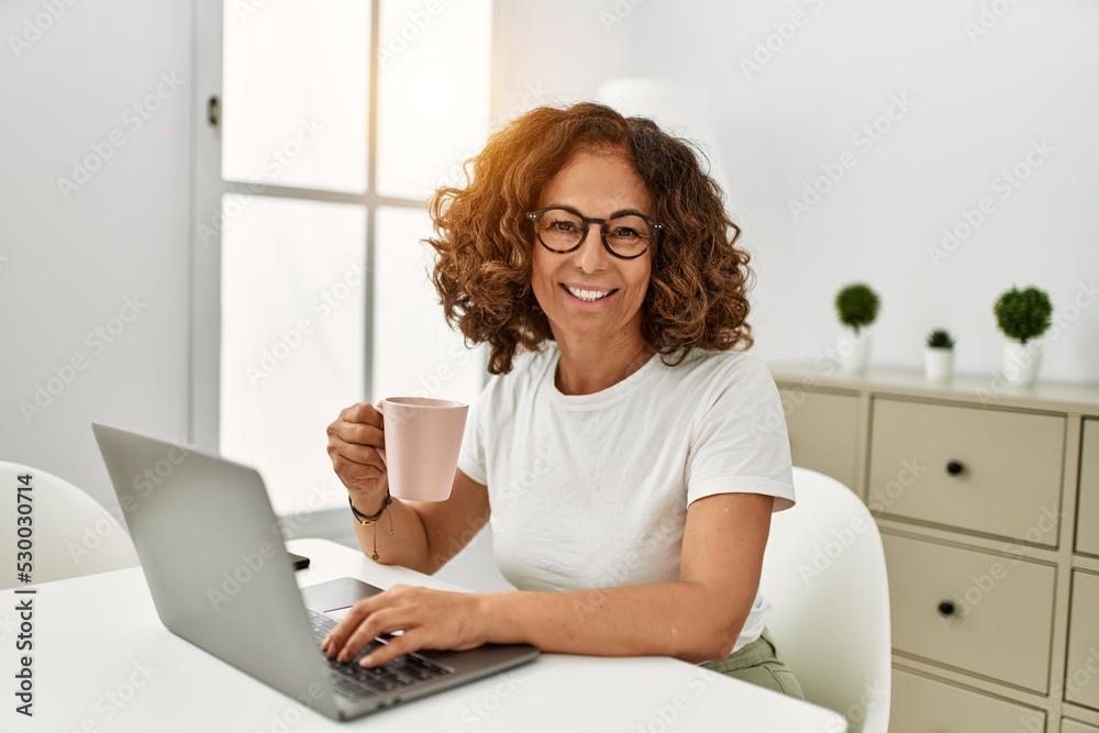 Wall mural middle age hispanic woman smiling confident using laptop at home