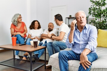 Group of middle age friends sitting on the sofa speaking. Man smiling happy talking on the smartphone at home.