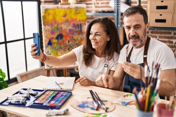 Obraz na płótnie Canvas Middle age man and woman artists drawing on notebook make selfie by the smartphone at art studio