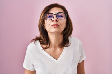 Fototapeta premium Middle age hispanic woman standing over pink background looking at the camera blowing a kiss on air being lovely and sexy. love expression.