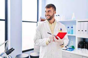 Naklejka na ściany i meble Young hispanic man wearing scientist uniform using touchpad at laboratory