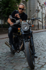 Obraz na płótnie Canvas Shot of man biker with his custom motorcycle at street in alley looking at camera.