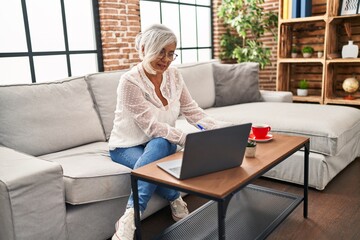 Middle age woman studying using laptop writing on book at home