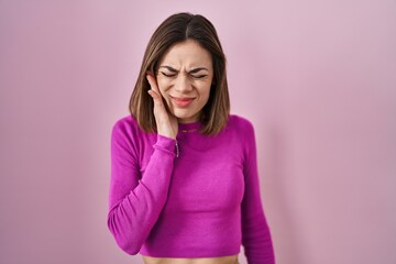 Fototapeta premium Hispanic woman standing over pink background touching mouth with hand with painful expression because of toothache or dental illness on teeth. dentist