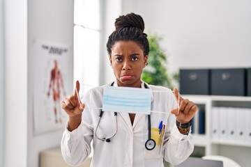 Young african american with braids wearing doctor uniform holding safety mask depressed and worry for distress, crying angry and afraid. sad expression.