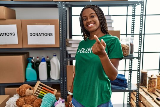 Young african american woman working wearing volunteer t shirt at donations stand beckoning come here gesture with hand inviting welcoming happy and smiling