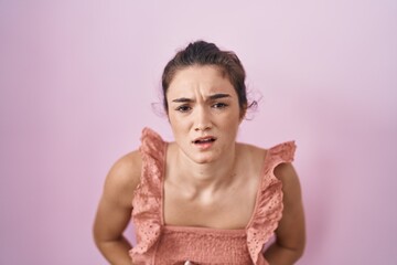 Young teenager girl standing over pink background with hand on stomach because indigestion, painful illness feeling unwell. ache concept.