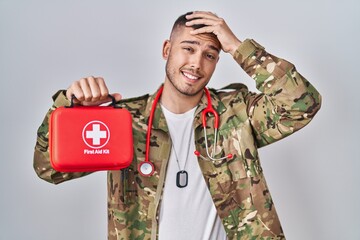 Young hispanic doctor wearing camouflage army uniform holding first aid kit stressed and frustrated...