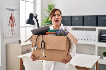 Middle age doctor woman holding cardboard box with items at the clinic angry and mad screaming frustrated and furious, shouting with anger. rage and aggressive concept.