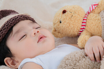Asian adorable newborn baby wear brown knit hat deeply sleeping with beige blanket next to teddy...