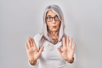 Middle age woman with grey hair standing over white background moving away hands palms showing...