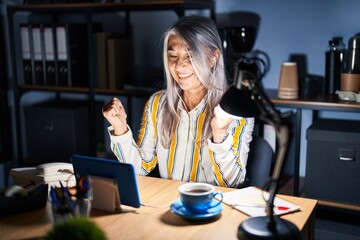 Middle age woman with grey hair working at the office at night celebrating surprised and amazed for success with arms raised and open eyes. winner concept.