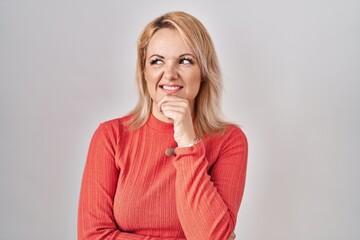 Blonde woman standing over isolated background thinking worried about a question, concerned and nervous with hand on chin
