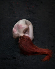 A naked red-haired woman in a creepy pose is lying on the ground. No face visible. The concept of...