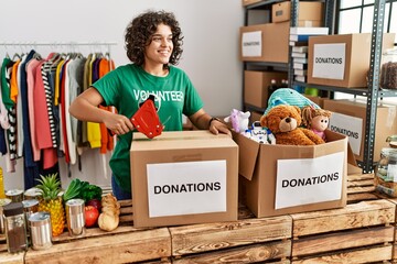 Young hispanic woman wearing volunteer uniform packing donations box at charity center
