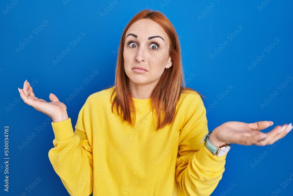 Sticker young woman standing over blue background clueless and confused expression with arms and hands raise