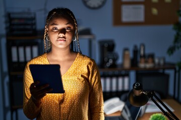 African american woman with braids working at the office at night with tablet looking sleepy and...