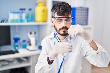 Young hispanic man scientist mixing liquid on glass at laboratory