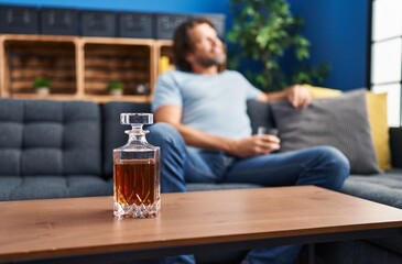 Middle age man drinking glass of whisky sitting on sofa at home