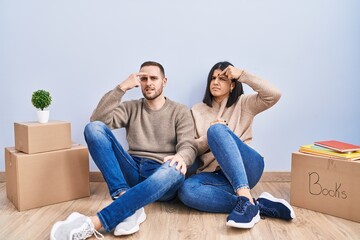 Young couple moving to a new home pointing unhappy to pimple on forehead, ugly infection of...