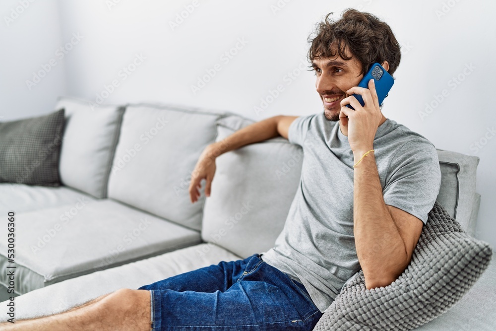 Sticker Young hispanic man smiling confident talking on thesmartphone at home