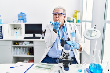 Senior caucasian man working at scientist laboratory looking at the camera blowing a kiss with hand on air being lovely and sexy. love expression.