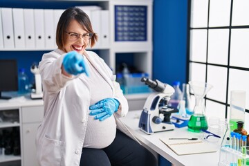 Pregnant woman working at scientist laboratory pointing displeased and frustrated to the camera, angry and furious with you