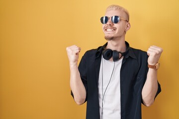 Young caucasian man wearing sunglasses standing over yellow background celebrating surprised and amazed for success with arms raised and eyes closed. winner concept.