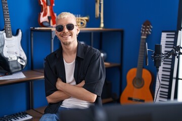 Young caucasian man artist sitting with arms crossed gesture at music studio