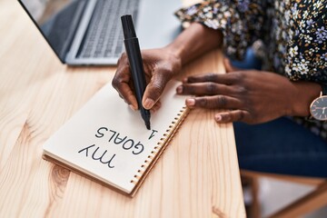 African american woman ecommerce business worker using laptop writing on notebook at office
