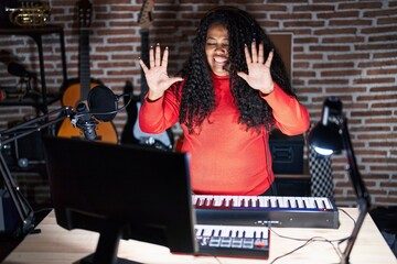 Plus size hispanic woman playing piano at music studio showing and pointing up with fingers number ten while smiling confident and happy.