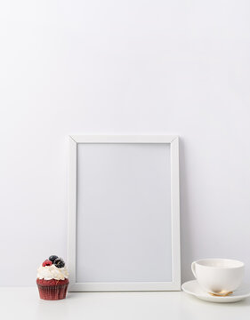 Art photo frame mockup with cup of coffee and cupcake, white background