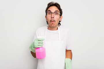 Young cleaner hispanic man isolated on white background shrugs shoulders and open eyes confused.