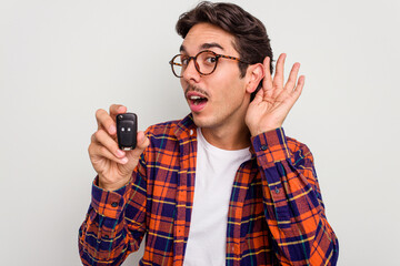Young hispanic man holding car keys isolated on white background trying to listening a gossip.