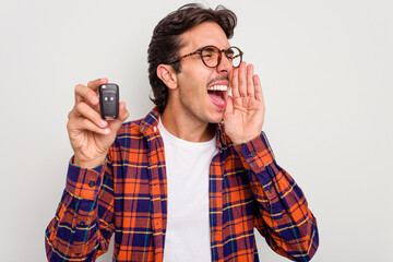 Young hispanic man holding car keys isolated on white background shouting and holding palm near opened mouth.