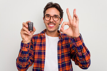 Young hispanic man holding car keys isolated on white background cheerful and confident showing ok...