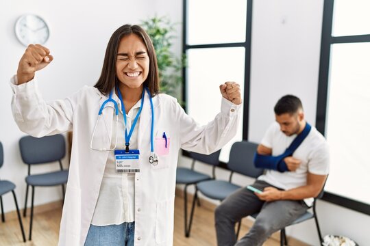 Young asian doctor woman at waiting room with a man with a broken arm very happy and excited doing winner gesture with arms raised, smiling and screaming for success. celebration concept.