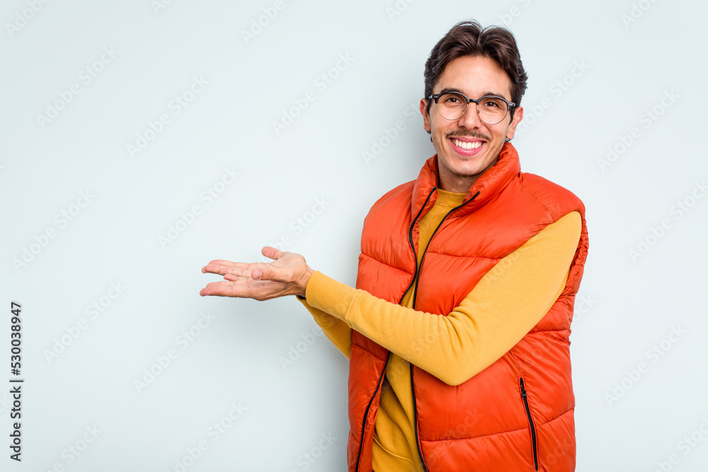 Wall mural young hispanic man isolated on blue background holding a copy space on a palm.