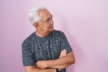 Middle age man with grey hair standing over pink background looking to the side with arms crossed convinced and confident